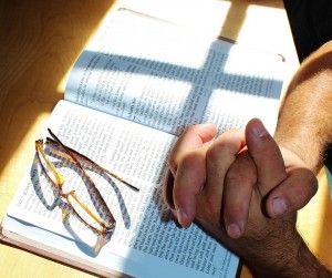 Stock art of someone with their hands clasped on an open bible