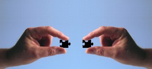 Stock photo of two hands putting two black puzzle pieces together
