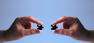 Stock photo of two hands putting two black puzzle pieces together