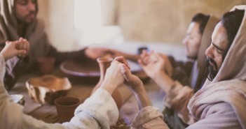 Stock photo of a group of Middle Eastern men holding hands and praying around a table