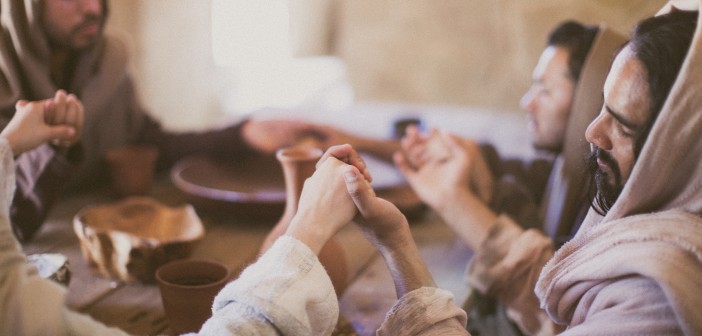 Stock photo of a group of Middle Eastern men holding hands and praying around a table