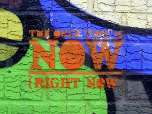 Stock photo of graffiti on a concrete wall that reads "the only time is NOW (right now)