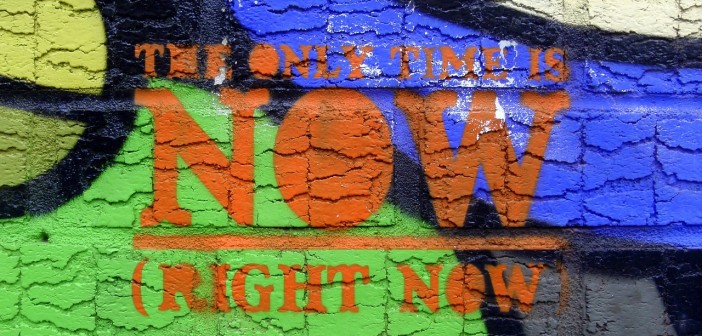 Stock photo of graffiti on a concrete wall that reads "the only time is NOW (right now)