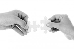 Black and white stock photo of two individuals putting two puzzle pieces together