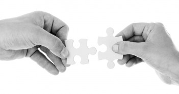 Black and white stock photo of two individuals putting two puzzle pieces together