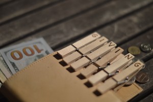 Stock photo of a wallet full of $100 bills and coins and a group of clothespins that spell out "GIVING"