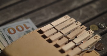 Stock photo of a wallet full of $100 bills and coins and a group of clothespins that spell out "GIVING"