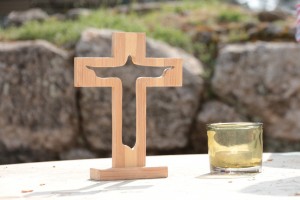 Stock photo of an outdoor altar with a small, wooden cross with a silhouette of Jesus cut out of it and a lit votive candle to its right