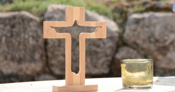 Stock photo of an outdoor altar with a small, wooden cross with a silhouette of Jesus cut out of it and a lit votive candle to its right