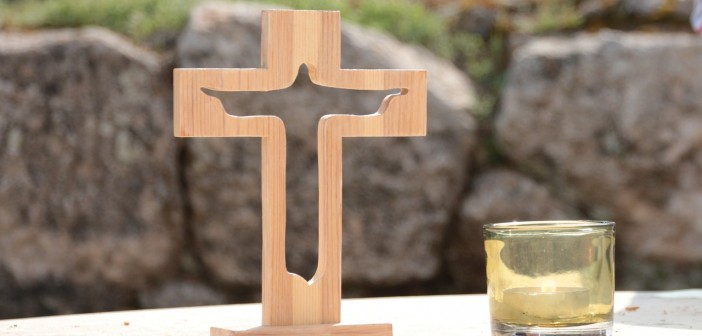 Stock photo of an outdoor altar with a small, wooden cross with a silhouette of Jesus cut out of it and a lit votive candle to its right