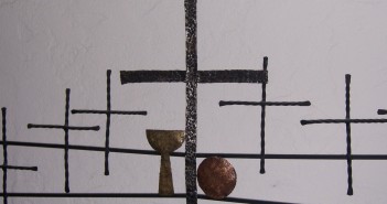 Stock photo of six black, hammered metal crosses with a gold hammered chalice and a copper hammered communion plate