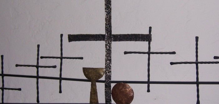 Stock photo of six black, hammered metal crosses with a gold hammered chalice and a copper hammered communion plate
