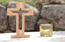 Wooden cross and a candle atop a table