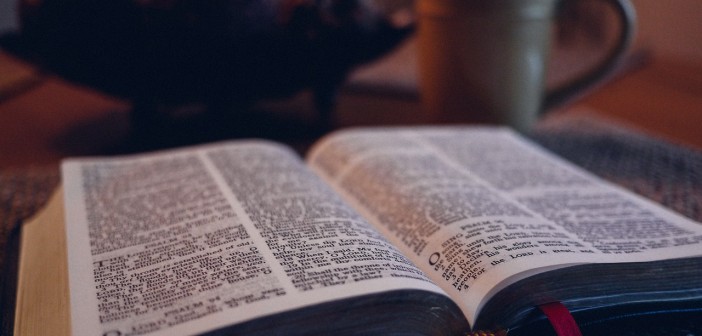 Stock photo of an open bible on a table with a coffee mug in the background