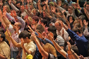 Stock photo of a large group of white people extending their arms upward during worship
