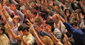 Stock photo of a large group of white people extending their arms upward during worship