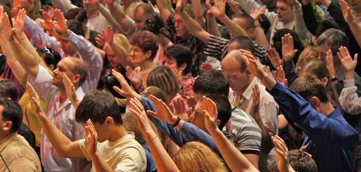 Stock photo of a large group of white people extending their arms upward during worship