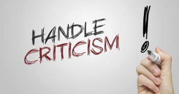 Stock photo of a hand writing "HANDLE CRITICISM!" on a whiteboard