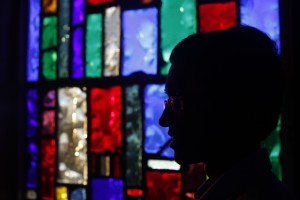 Stock photo of a silhouette of an individual sitting in a room back-lit by stained glass windows