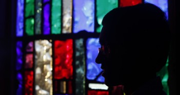 Stock photo of a silhouette of an individual sitting in a room back-lit by stained glass windows