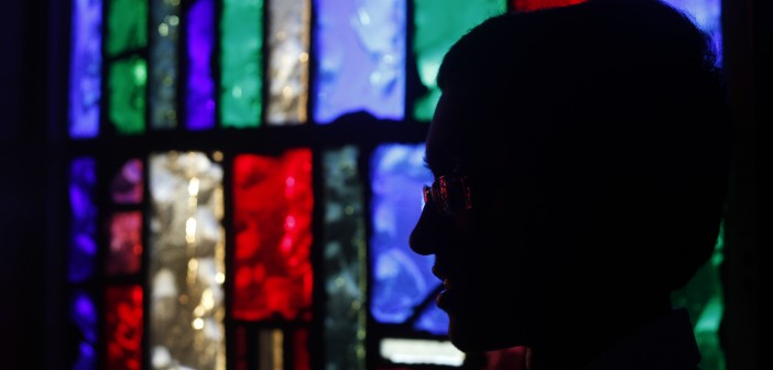 Stock photo of a silhouette of an individual sitting in a room back-lit by stained glass windows