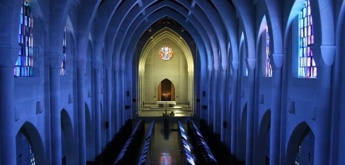 Stock photo of the interior of an empty sanctuary with the lights turned off and sunlight pouring in through the stained-glass windows