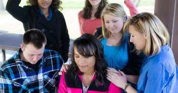 Stock photo of a group of young individuals of mixed genders and races praying over one of their peers