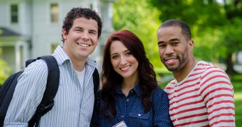 Stock photo of three young individuals - a white man, a white woman, and an African American man - posing for a portrait outside of a house