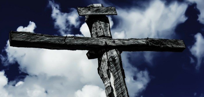 Stock photo of a cross against a blue sky with some white fluffy clouds