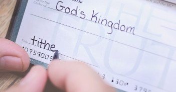 Stock photo of someone writing a check of an unspecified amount made out to "God's Kingdom" with "tithe" in the memo line