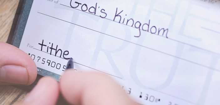 Stock photo of someone writing a check of an unspecified amount made out to "God's Kingdom" with "tithe" in the memo line