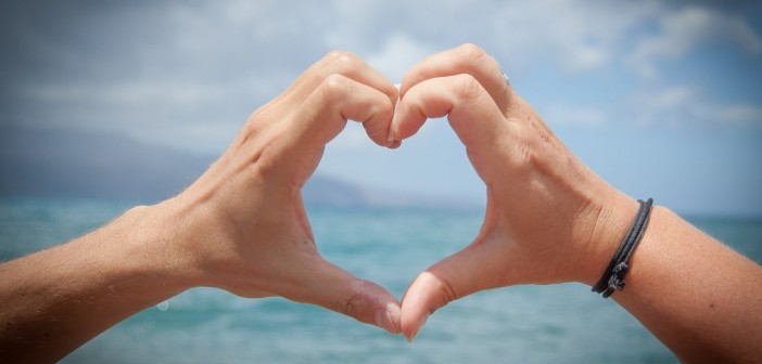 Stock photo of a pair of hands forming a heart looking out over a body of water