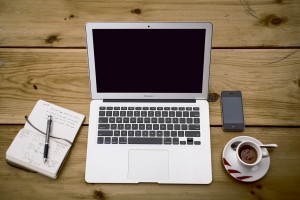 Stock photo of someone's workspace that has a moleskine notebook, a MacBook Air, an iPhone, and a cup of espresso