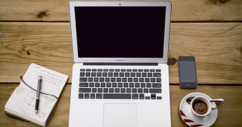 Stock photo of someone's workspace that has a moleskine notebook, a MacBook Air, an iPhone, and a cup of espresso