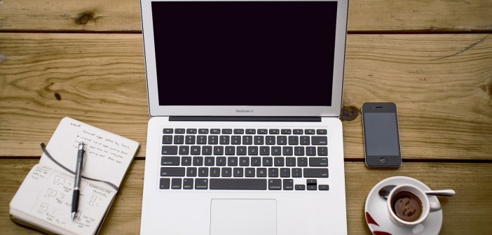 Stock photo of someone's workspace that has a moleskine notebook, a MacBook Air, an iPhone, and a cup of espresso