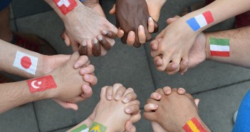 Stock photo of a diverse group of interlocked hands with different flags painted on their wrists