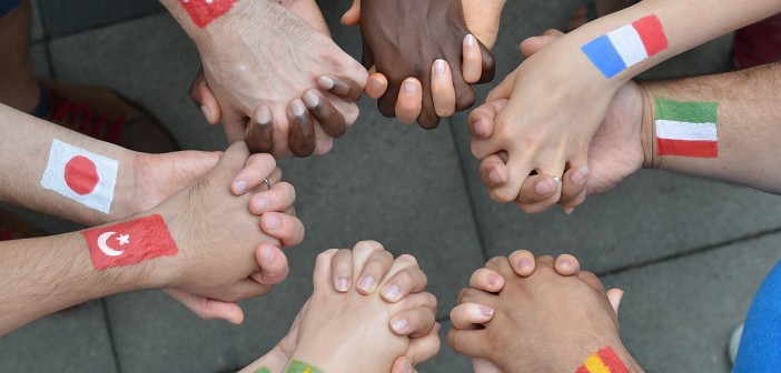Stock photo of a diverse group of interlocked hands with different flags painted on their wrists