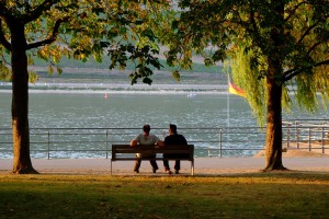 Stock photo of two people on a bench in a park by a waterfront in Germany