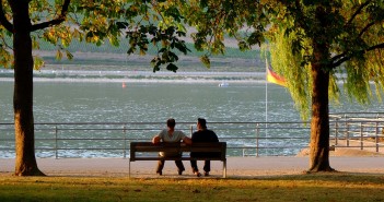 Stock photo of two people on a bench in a park by a waterfront in Germany