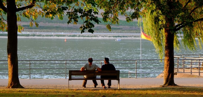 Stock photo of two people on a bench in a park by a waterfront in Germany
