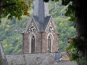 Stock photo of a steeple/bell tower with a clock on it in the mountains. It is approximately 4:10 in the afternoon.