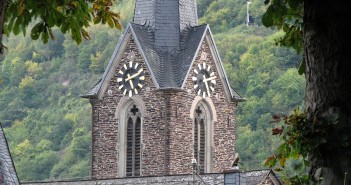 Stock photo of a steeple/bell tower with a clock on it in the mountains. It is approximately 4:10 in the afternoon.