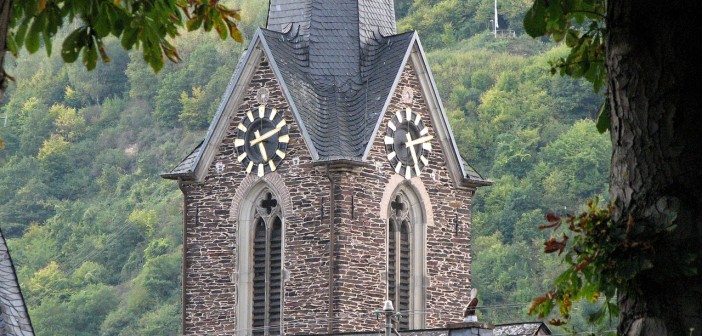 Stock photo of a steeple/bell tower with a clock on it in the mountains. It is approximately 4:10 in the afternoon.