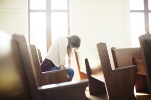 Stock photo of a young white woman praying by herself in a pew