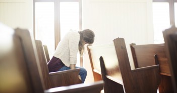 Stock photo of a young white woman praying by herself in a pew