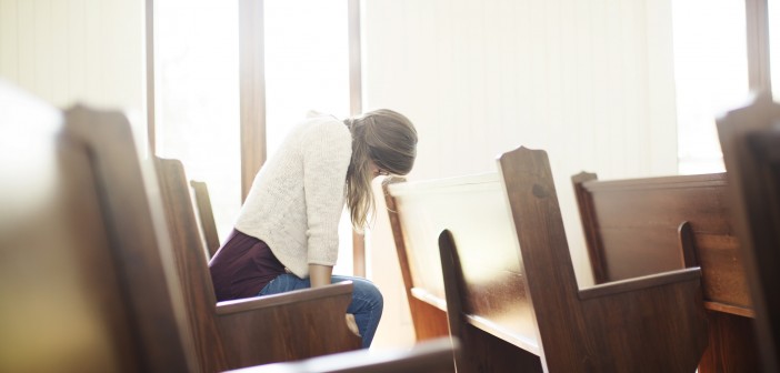 Stock photo of a young white woman praying by herself in a pew