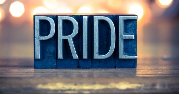 Stock photo of the word "PRIDE" carved out of wood and painted silver