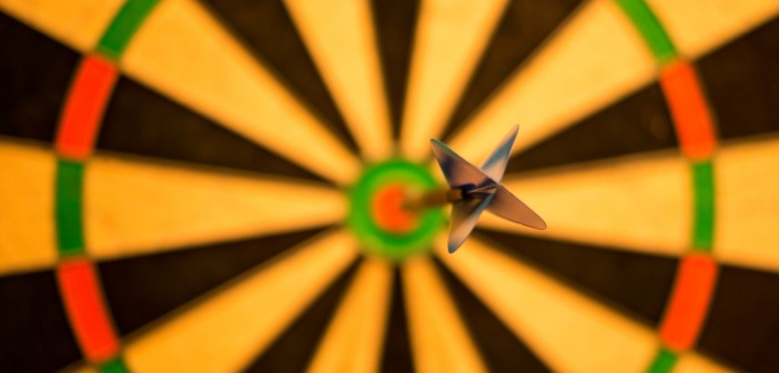 Stock photo of an empty, out-of-focus dartboard save for one, lone, in-focus dart on the bulls-eye