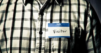 An Open Letter to Churches Seeking New Members Photo of an individual wearing a black-and-white checkered shirt and a nametag that reads "hello my name is VISITOR"