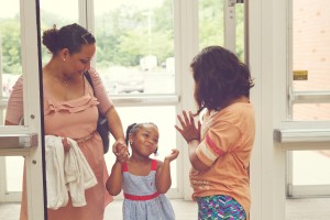 Stock photo of three Latina women of different ages - one middle age, one child, and one teenager - greeting each other at a door